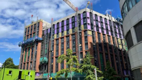 A partially-built student accommodation block is surrounded by cranes