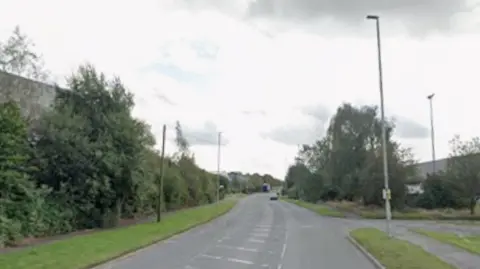 Google A Google Streetview of Regs Way. Industrial units and trees can be seen either side of the road.
