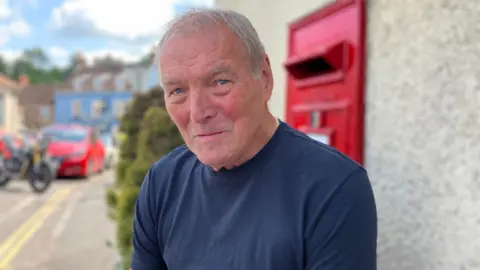 Jim Beacham sitting in front of a post box in Pensford