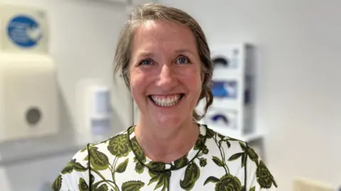 Consultant Radiologist and study lead Dr Lyn Jones smiling into the camera. She is stood in a medical setting/room.