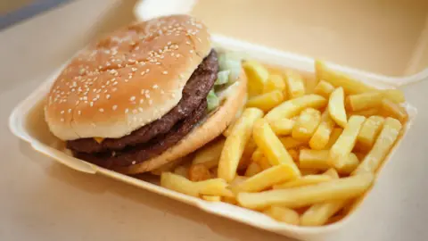 A photo showing a takeaway carton containing a burger in a bun and a portion of chips