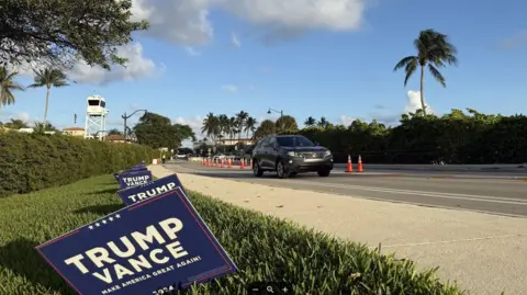 Stephen Greaves/BBC News A car drives past Mar-a-Lago - there are signs for the Trump Vance campaign on the edge of the lawn and the control tower of the US Secret Service can be seen in the distance.