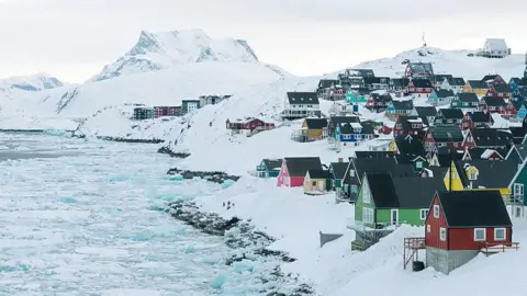 Getty Images Homes on the Greenland coast, surrounded by snow and sea ice and mountains