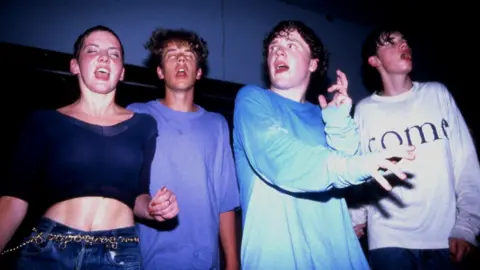 Getty Images Four people in t-shirts dancing in the dark captured on a flash camera inside the club.