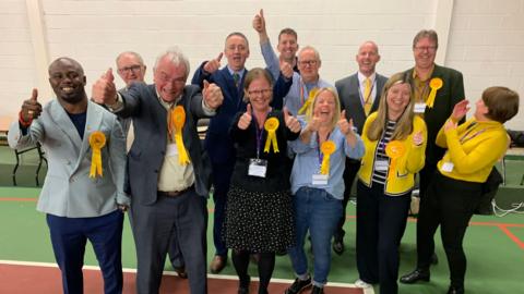 Image of the Liberal Democrat members and councillors celebrating their win, wearing yellow rosettes