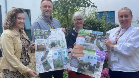 NWAFT People involved in the project holding big charts displaying the artist's design of the garden, smiling for the camera