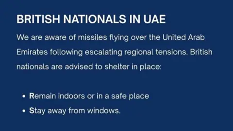 A blue notification for British Nationals in UAE, which in white writing reads: We are aware of missiles flying over the United Arab Emirates following escalating regional tensions. British nationals are advised to shelter in place: Remain indoors or in a safe place. Stay away from windows.