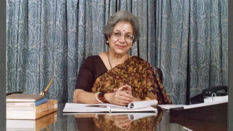 Courtesy: NCPA Library Archives A photo of Vijaya Mehta sitting at her desk in her office and writing in a book.