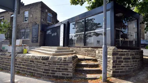 The site in Horton Park Avenue shows a closed gift shop to the left with an extension stretching across the mid-height stone terrace.