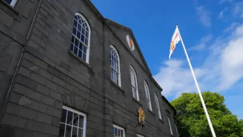 A grey stone States of Guernsey building, with a white flagpole.