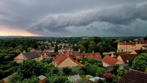 BBC Weather Watchers - BOA G A long ridge-shaped bank of dark grey cloud is seen above the houses of a village