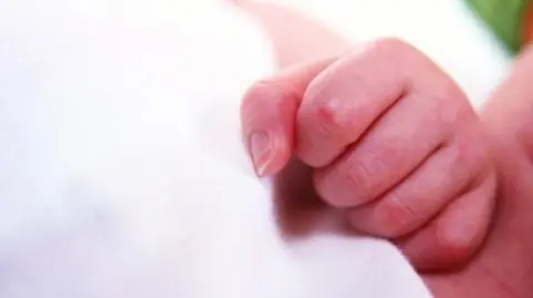 The pink and red clenched fist of a newborn baby against a white blanket