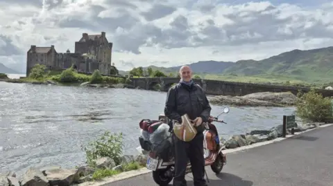 A biker with a scooter in front of Ellan Donan Castle in the Highlands