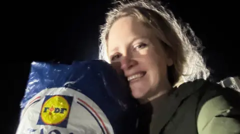 Laura Poole Photo of Laura who has long blonde hair and smiling. She is posing next to the bag of clothes which are inside a Lidl carrier bag.