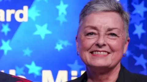 City of Wolverhampton Council A woman with short grey hair and a dark jacket in a room with blue and white lights in the background