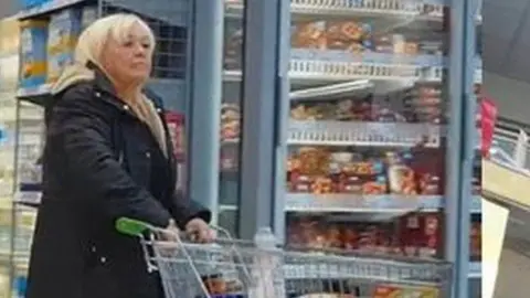 CPS Surveillance footage of Christina Pomfrey, who has short blonde hair and is wearing a thick black coat, pushing a trolley along a supermarket aisle