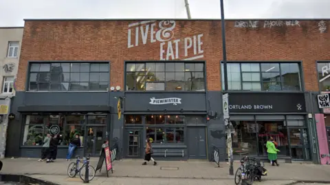 Pieminister in Bristol. The building is red brick with Live & Eat Pie painted at the top. The storefront is black with a white Pieminister logo above the door. 