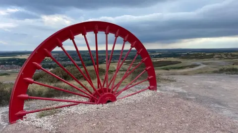 The red winding wheel from the shaft at Thoresby Colliery has been sunk into the ground at the top of Thoresby Vale Country Park