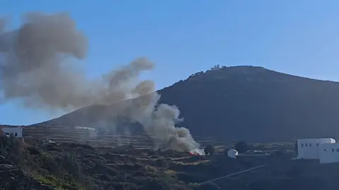 Large plume of grey smoke seen coming from a crash site, with a large mountain in the background