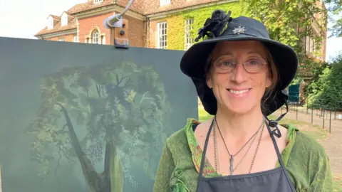 Sam Read/BBC Claire Valentine-Gibson next to her painting of the tree