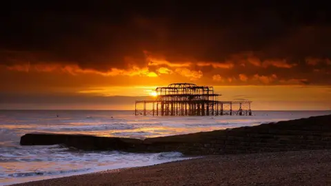 Getty Images A ruined pier out at sea. The sun is setting. 