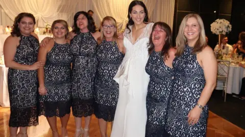 Debbie Speranza Six wedding guests in identical dresses pose for a photograph with the bride