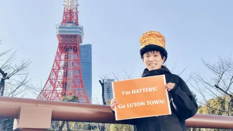 Sweets Nanako Sweets Nanako holding a sign that says "I'm Hatters, Go Luton Town" outside Tokyo tower