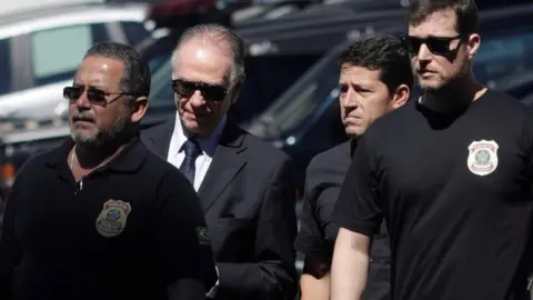 Reuters The President of the Brazilian Olympic Committee pictured between federal officers, wearing a suit and sunglasses
