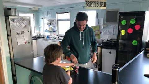 man giving a pop and crisps to a boy in the KPC tuck shop