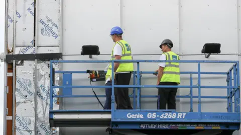 Getty Images Workers remove cladding for testing from a tower blocks in Salford City