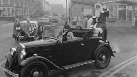 MNH Santa Claus sitting on the back of a car