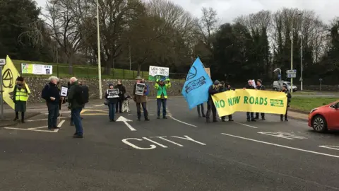 BBC Extinction Rebellion protesters holding up 'No New Roads' banner and blocking the roundabout near Norfolk County Hall