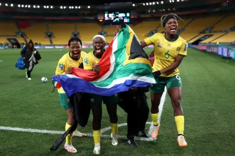 Catherine Ivill/Getty Images Female footballers holding South African flag on 2 August 2023