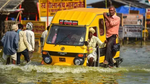 Getty Images People wade through a flooded path near Sangam, the confluence of the Ganges, Yamuna and mythical Saraswati rivers after the water level of river Ganges and river Yamuna rose, in Allahabad on October 14, 2022.