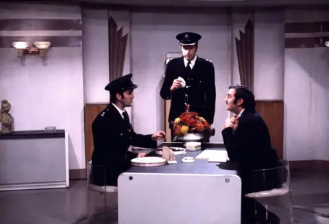 Monty Python John Cleese as Inspector Praline, Graham Chapman as Superintendent Parrot, and Terry Jones as Mr Milton in the Crunchy Frog sketch.