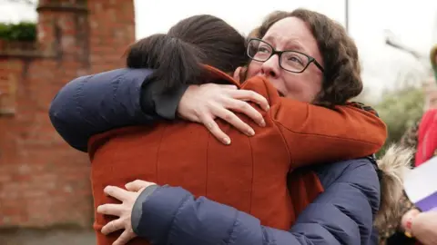 PA Media Rhiannon Davies (left) embraces Kayleigh Griffiths, following the release of the final report by Donna Ockenden