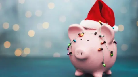 Getty/CatLane Christmas Savings Background with Pink Piggy Bank Wearing Santa Hat - stock photo