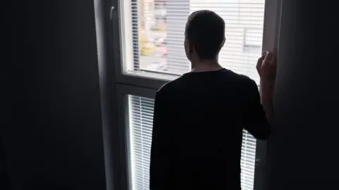 Tero Vesalainen Anonymous man gazes out of a window with his back facing the camera.