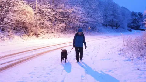 PA Media A woman walks her dog in the snow in Hexham on Monday morning