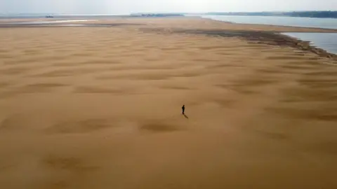 AFP In this aerial view environmentalist Luis Martinez walks along a sand bank at the Parana River, during a historic drought, near Paso de la Patria, Corrientes, Argentina, on August 20, 2021.