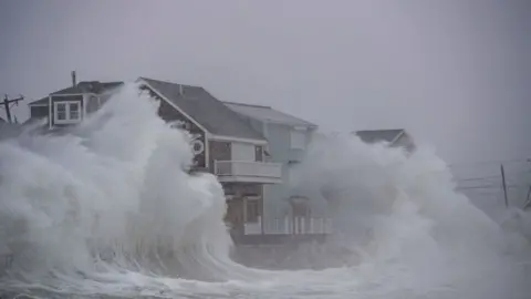 Getty Images Waves crash over oceanfront homes during a noreaster in Scituate, Massachusetts on January 29, 2022. - Blinding snow whipped up by near-hurricane force winds pummeled the eastern United States