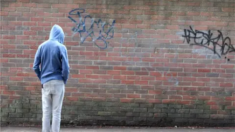 Getty Images teenager in hoodie standing by graffitied wall