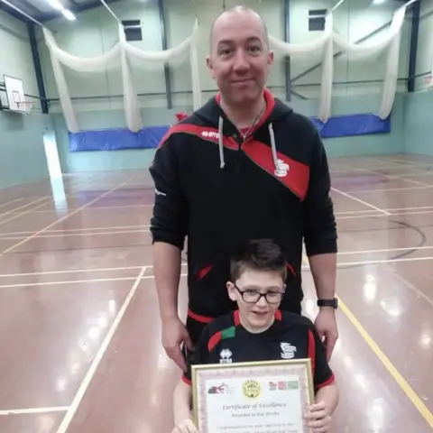 family photo Coach Lee Coulson and a young Kai holding a certificate