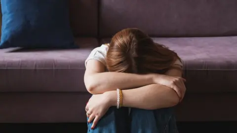 Getty Images A woman with her head in her hands leaning against a sofa