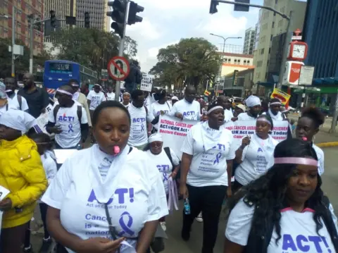 BBC Protesters in Nairobi walk down a street, carrying banners and wearing matching T-shirts.