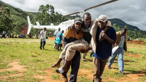 AFP A man injured in the cyclone in Zimbabwe is carried away from a helicopter.