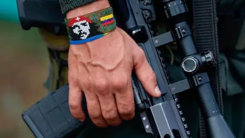 A man wearing a bracelet with the colours of the Colombian flag and a picture of Che Guevara holds a rifle at a gathering of FARC dissident guerrilla holding a rifle, in Casa Roja, Colombia, 16 April 2023