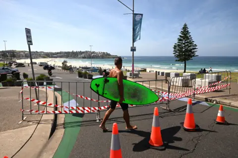 Getty Images A surfer walks in front of a fence near Bondi Beach