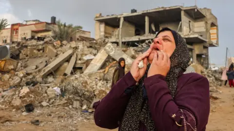 A Palestinian woman reacts as people inspect the damage after Israeli strikes on Rafah, on the southern Gaza Strip, in November 2023