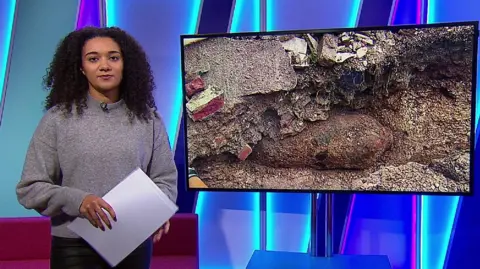 Newsround presenter Nina Blissett in front of a screen showing an unearthed unexploded WW2 bomb.